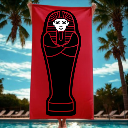 Red towel with black mummy design held by a person against a poolside background with palm trees.
