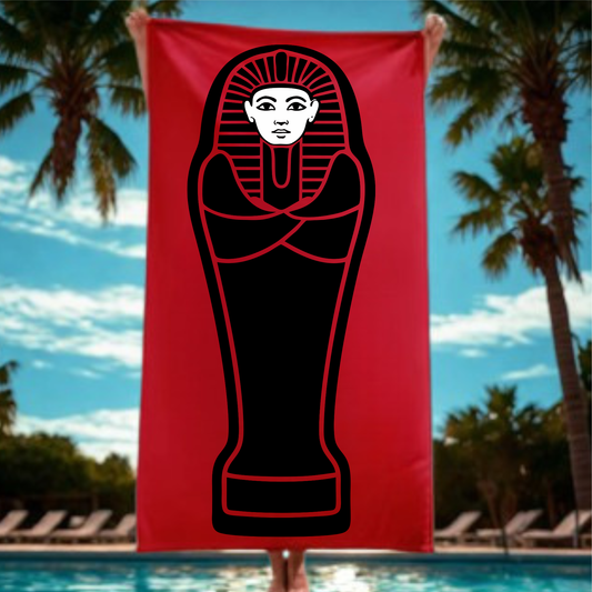 Red towel with black mummy design held by a person against a poolside background with palm trees.