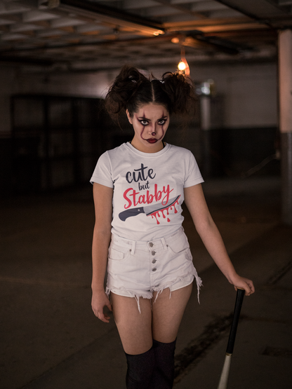 Person wearing a t-shirt with 'cute but stabby' text and a knife graphic in a dimly lit room.