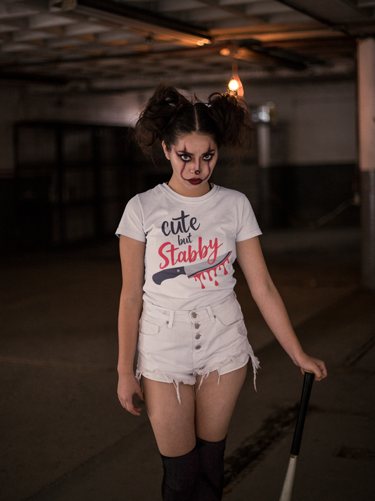 Person wearing a t-shirt with 'cute but stabby' text and a knife graphic in a dimly lit room.