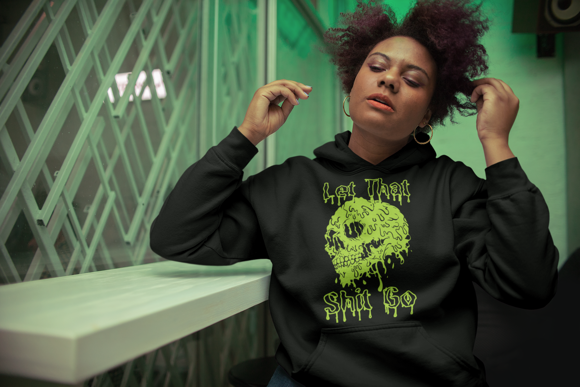A person wearing a black hoodie with a green melting skull with the words let that shit go.