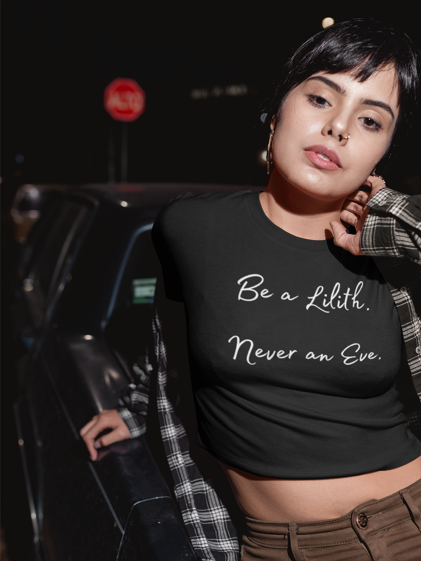 Woman wearing a black t-shirt with text that says 'be a Lilith never an eve', standing outdoors at night.
